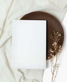 a blank paper on top of a brown plate with dried flowers and a white card