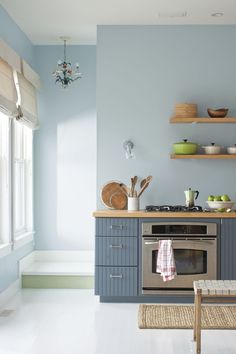 a kitchen with blue walls and white flooring has an oven in the center, shelves above it