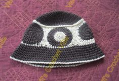 a crocheted black and white hat sitting on top of a purple bedspread