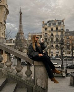 a woman sitting on top of a stone railing next to a building with the eiffel tower in the background