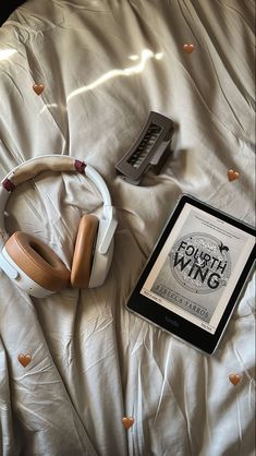 an electronic device and headphones are on a bed with white sheets that have hearts scattered around them