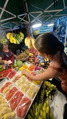 a woman standing in front of a table filled with lots of fruits and veggies