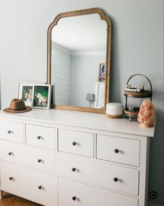 a white dresser with a large mirror and pictures on it