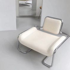 a white chair sitting on top of a gray floor next to a wall with a mirror