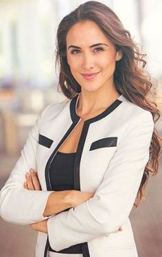 a woman standing with her arms crossed and looking at the camera while wearing a white blazer