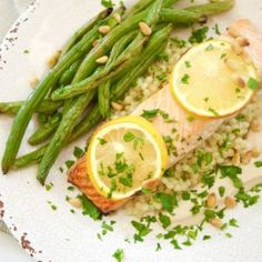 a white plate topped with fish and asparagus next to lemon slices on top of rice