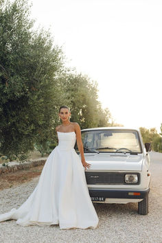 a woman in a wedding dress standing next to a car