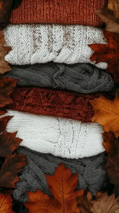 four knitted sweaters and autumn leaves on the ground with one folded in half