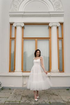 a woman wearing a white dress standing in front of a window