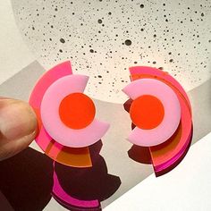 "Deconstruct your style with these modern geometric studs. A modern take on the Art Deco aesthetic, these abstracted eyes in a concentric arrangement will add color blocking to your outfit. Bold with a neon pink/orange backing, these earrings project a bright light effect that is sure to make a statement. Made from 1/8\" thick acrylic, these earrings are made of solid construction with a mixture of solid and clear acrylic pieces that let light through. Each earring measures approximately 1-3/8 i Modern Geometric Earrings, Modern Handmade Geometric Earrings, Handmade Modern Geometric Earrings, Modern Multicolor Earrings With Bold Design, Bold Geometric Earrings With Bold Design, Bold Geometric Designed Earrings, Pink Geometric Earrings, Bold Geometric Earrings, Bold Handmade Geometric Earrings