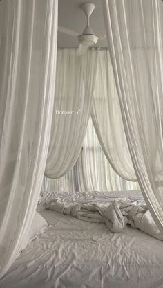 an unmade bed with white drapes and pillows