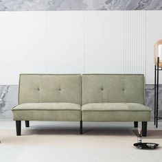 a green couch sitting on top of a white floor next to a black table and lamp