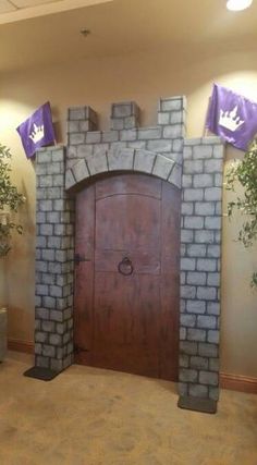 a large wooden door in the middle of a room with purple flags hanging from it's sides