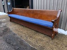 an old wooden bench with blue cushion on the bottom and side, in front of a building