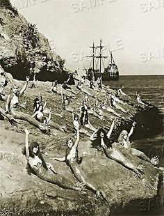 black and white photograph of people doing yoga on rocks near the ocean with a ship in the background