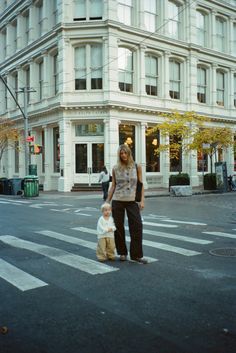 a woman and child crossing the street in front of a building