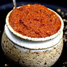 a bowl filled with chili sauce sitting on top of a black table next to spices