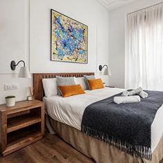 a bedroom with white walls and wood flooring has a large painting on the wall above the bed