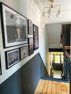 a hallway with pictures on the wall and wooden flooring, along with stairs leading up to another room