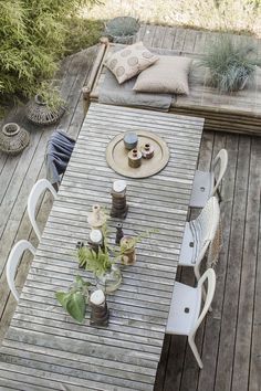 an outdoor table and chairs on a wooden deck with potted plants in vases