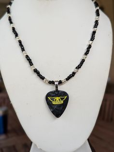 a necklace with a guitar pick shaped pendant on it's side and black beads around the neck