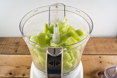 a food processor filled with green fruit on top of a wooden table