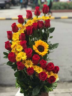 a vase filled with red roses and yellow flowers