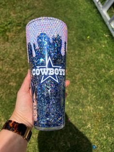 someone holding up a tumbler cup with the word cowboys on it in front of some grass