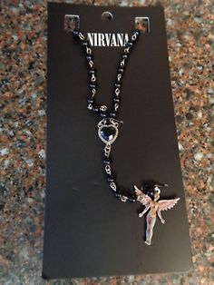 a black and white necklace with a silver angel charm on it's side, sitting in front of a box