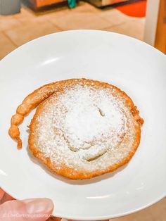 a powdered pastry on a white plate being held up by someone's hand