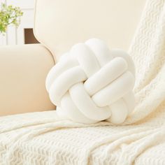 a large white knot pillow sitting on top of a couch next to a beige chair