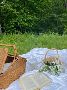 an open book and wicker basket sitting on a blanket in front of some trees