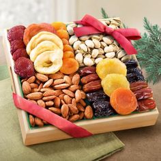 an assortment of nuts and dried fruits in a wooden tray with red ribbon on top