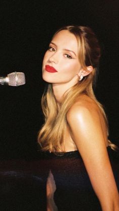 a woman in a black dress is holding a microphone and looking into the distance with red lipstick on her lips