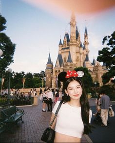 a woman standing in front of a castle with a minnie mouse ears on her head