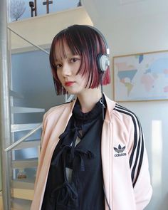 a woman with red hair wearing headphones standing in front of a stair case and looking at the camera