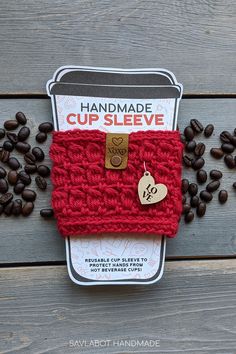 the coffee cup sleeve is knitted in red yarn and has a heart charm on it