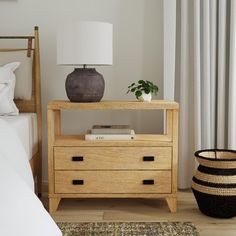 a bedroom with a bed, nightstand and lamp on it's side table in front of a window