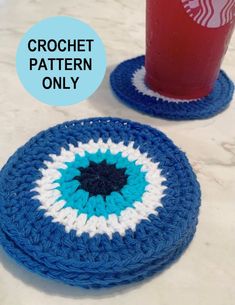 two crocheted coasters on a table next to a red cup