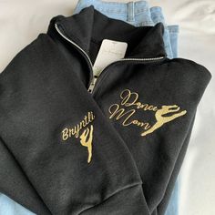 a pair of black sweatshirts with gold lettering on the front and back, sitting on top of a bed