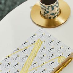 a white table topped with a cup of coffee next to a gold pen and notebook