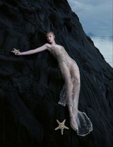 a woman laying on top of a rock next to the ocean