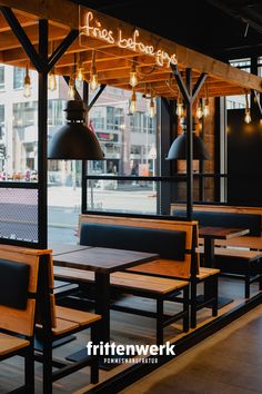 an empty restaurant with wooden tables and black leather seats, lights hanging from the ceiling