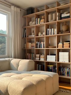 a white couch sitting in front of a window next to a book shelf filled with books