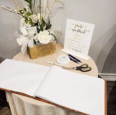 an open book sitting on top of a table next to a vase with white flowers