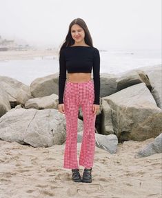 a woman standing on top of a sandy beach next to the ocean wearing red and white checkered pants