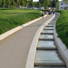 several people walking down a path with water cascading on the sides and green grass in the background