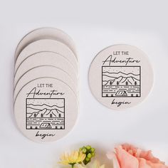 four white coasters with the words let the adventure begin on them next to flowers