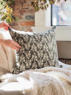 a person is holding a pillow on a couch in front of a brick wall and window