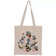 a white tote bag with blue and red flowers on the front, and a bee flying over it